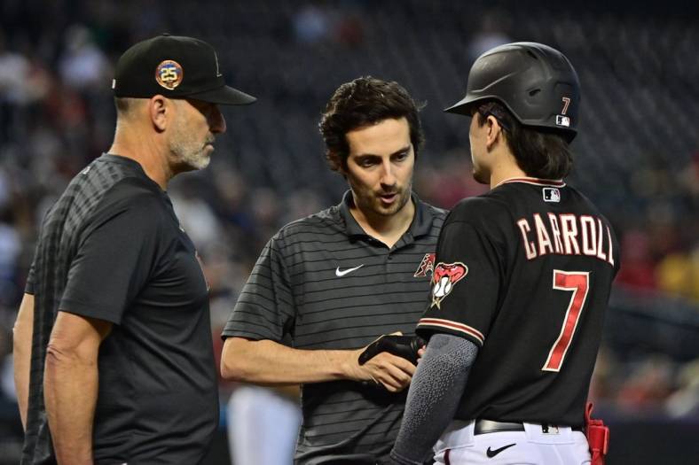 Sep 6, 2023; Phoenix, Arizona, USA; Arizona Diamondbacks left fielder Corbin Carroll (7) has his hand examined by a trainer as manager Torey Lovullo (17) looks on in the fourth inning against the Colorado Rockies at Chase Field. Mandatory Credit: Matt Kartozian-USA TODAY Sports