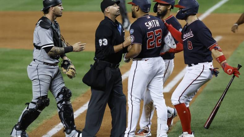 Sep 18, 2023; Washington, District of Columbia, USA; Washington Nationals first baseman Dominic Smith (22) is restrained from Chicago White Sox starting pitcher Mike Clevinger (not pictured) after hitting a home run by home plate umpire Will Little (93) as White Sox catcher Yasmani Grandal (24) steps in during the ninth inning at Nationals Park. Mandatory Credit: Geoff Burke-USA TODAY Sports
