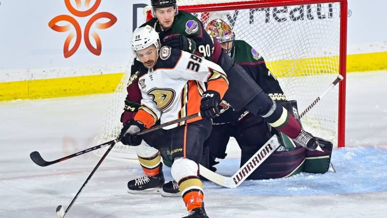 Oct 21, 2023; Tempe, Arizona, USA;  Anaheim Ducks center Sam Carrick (39) and Arizona Coyotes defenseman J.J. Moser (90) battle for position in front of goaltender Karel Vejmelka (70) in the first period at Mullett Arena. Mandatory Credit: Matt Kartozian-USA TODAY Sports