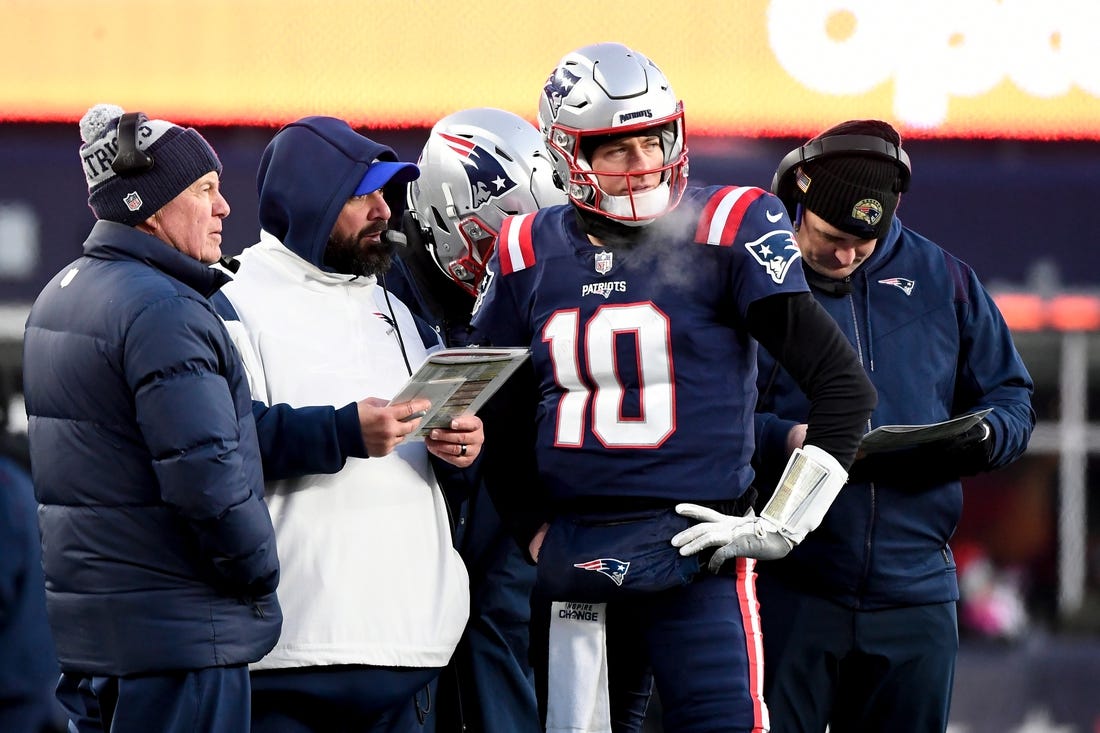 Dec 24, 2022; Foxborough, Massachusetts, USA; New England Patriots quarterback Mac Jones (10) checks with head coach Bill Belichick, left, and senior football advisor Matt Patricia, second from left, during the second half against the Cincinnati Bengals at Gillette Stadium. Mandatory Credit: Eric Canha-USA TODAY Sports