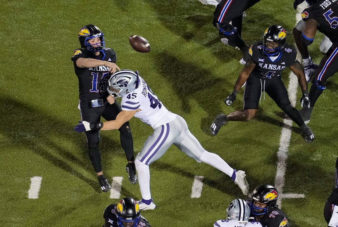 Nov 18, 2023; Lawrence, Kansas, USA; Kansas Jayhawks quarterback Cole Ballard (15) throws a touchdown pass as he is hit by Kansas State Wildcats linebacker Austin Romaine (45) during the first half at David Booth Kansas Memorial Stadium. Mandatory Credit: Jay Biggerstaff-USA TODAY Sports