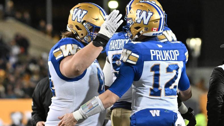 Nov 19, 2023; Hamilton, Ontario, CAN;  Winnipeg Blue Bombers quarterback Dakota Prukop (12) celebrates with offensive lineman Liam Dobson (64) after scoring a touchdown against the Montreal Alouettes in the first half at Tim Hortons Field. Mandatory Credit: Dan Hamilton-USA TODAY Sports