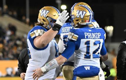 Nov 19, 2023; Hamilton, Ontario, CAN;  Winnipeg Blue Bombers quarterback Dakota Prukop (12) celebrates with offensive lineman Liam Dobson (64) after scoring a touchdown against the Montreal Alouettes in the first half at Tim Hortons Field. Mandatory Credit: Dan Hamilton-USA TODAY Sports