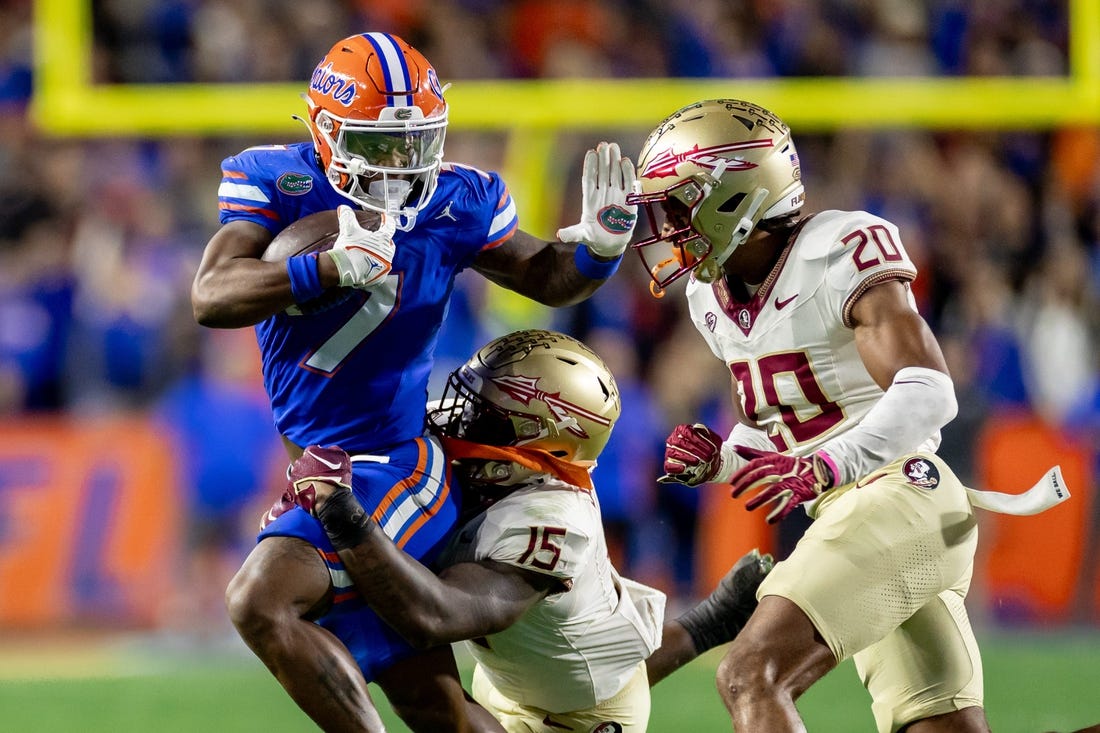 Florida Gators running back Trevor Etienne (7) rushes with the ball while Florida State Seminoles linebacker Tatum Bethune (15) and Florida State Seminoles defensive back Azareye'h Thomas (20) attempt to tackle during the first half at Steve Spurrier Field at Ben Hill Griffin Stadium in Gainesville, FL on Saturday, November 25, 2023. [Matt Pendleton/Gainesville Sun]