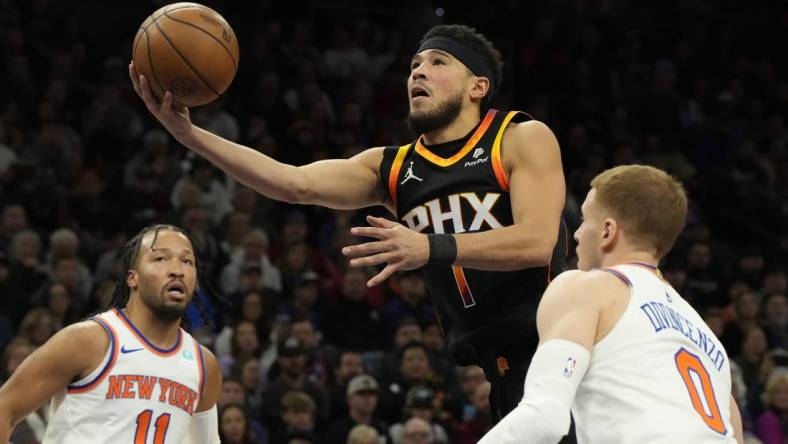 Dec 15, 2023; Phoenix, Arizona, USA; Phoenix Suns guard Devin Booker (1) drives between New York Knicks guard Jalen Brunson (11) and  guard Donte DiVincenzo (0) in the first half at Footprint Center. Mandatory Credit: Rick Scuteri-USA TODAY Sports