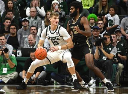 Dec 18, 2023; East Lansing, Michigan, USA;   Michigan State Spartans center Carson Cooper (15) dribbles the ball against Oakland Golden Grizzlies forward Tuburu Naivalurua (12) during the first half at Jack Breslin Student Events Center. Mandatory Credit: Dale Young-USA TODAY Sports