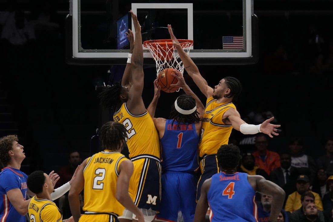 Dec 19, 2023; Charlotte, North Carolina, USA; Florida Gators guard Walter Clayton Jr. (1) is sandwiched at the basket by Michigan Wolverines forward Tarris Reed Jr. (32) and forward Olivier Nkamhoua (13) during the first half at Spectrum Center. Mandatory Credit: Jim Dedmon-USA TODAY Sports