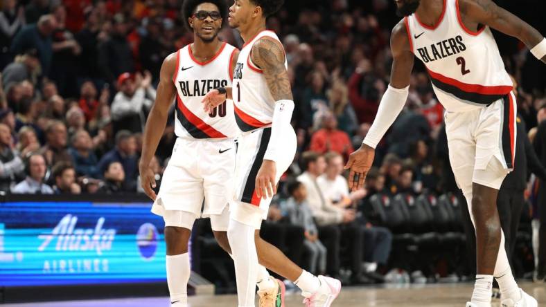 Dec 19, 2023; Portland, Oregon, USA;  Portland Trail Blazers guard Scoot Henderson (00), left, and center Deandre Ayton (2) celebrates with guard Anfernee Simons (1) after Simons scored a basket to seal the 109-104 win over Phoenix Suns at Moda Center. Mandatory Credit: Jaime Valdez-USA TODAY Sports