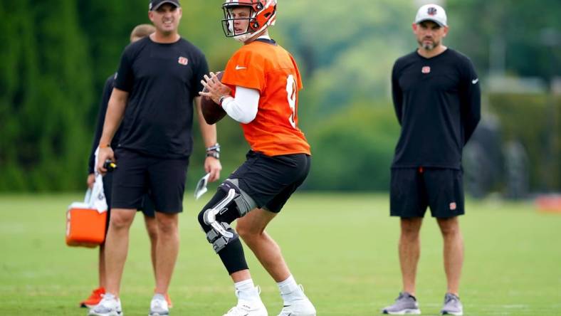 Cincinnati Bengals quarterback Joe Burrow (9) drops back to throw as Bengals coach Zac Taylor, left, and new offensive coordinator Dan Pitcher observe at the practice fields next to Paul Brown Stadium in Cincinnati.