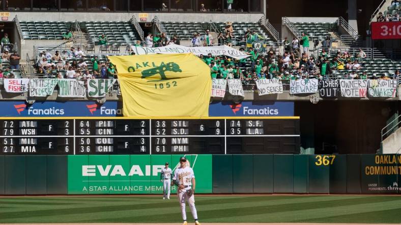 Sep 24, 2023; Oakland, California, USA; Fans in the outfield bleachers display homemade signs critical of the MLB Commissioner and Oakland Athletics ownership and Oakland Athletics infielder Zack Gelof (20) and outfielder Brent Rooker (25) stand on the field during the eighth inning against the Detroit Tigers at Oakland-Alameda County Coliseum. Mandatory Credit: Robert Edwards-USA TODAY Sports