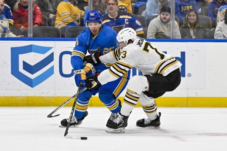 Jan 13, 2024; St. Louis, Missouri, USA;  St. Louis Blues center Jordan Kyrou (25) and Boston Bruins defenseman Charlie McAvoy (73) battle for the puck during the second period at Enterprise Center. Mandatory Credit: Jeff Curry-USA TODAY Sports