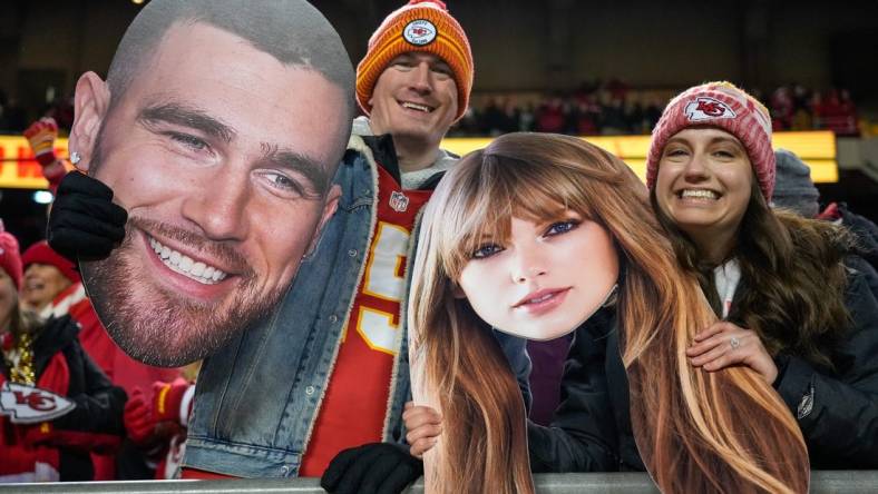 Chiefs fans wave Taylor Swift and Travis Kelce cutouts at Arrowhead Stadium.