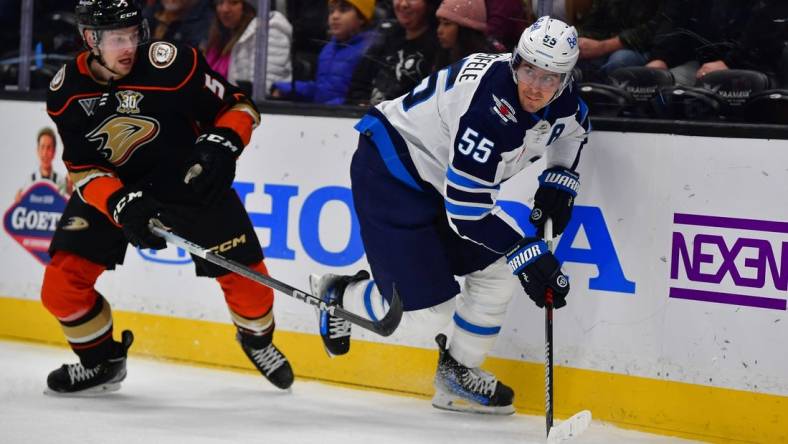 Jan 5, 2024; Anaheim, California, USA; Winnipeg Jets center Mark Scheifele (55) moves the puck ahead of Anaheim Ducks defenseman Urho Vaakanainen (5) during the first period at Honda Center. Mandatory Credit: Gary A. Vasquez-USA TODAY Sports