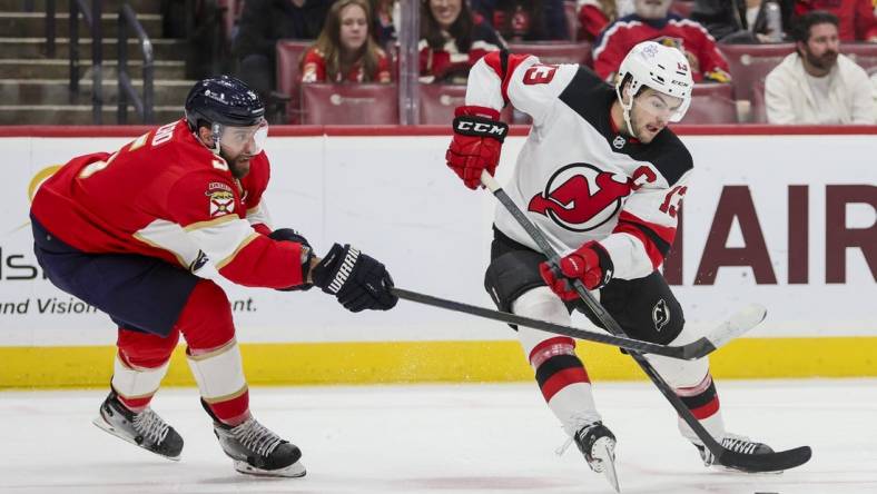 Jan 13, 2024; Sunrise, Florida, USA; New Jersey Devils center Nico Hischier (13) protects the puck from Florida Panthers defenseman Aaron Ekblad (5) during the first period at Amerant Bank Arena. Mandatory Credit: Sam Navarro-USA TODAY Sports