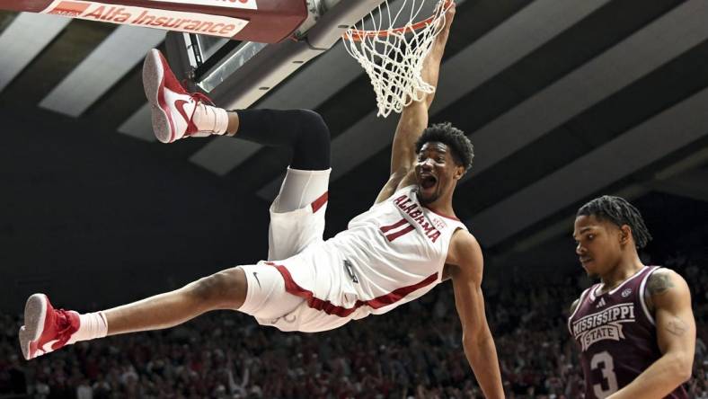 Feb 3, 2024; Tuscaloosa, Alabama, USA;  Alabama forward Mohamed Wague (11) hangs on the rim with a huge smile after dunking over Mississippi State guard Shakeel Moore (3) at Coleman Coliseum. Mandatory Credit: Gary Cosby Jr.-USA TODAY Sports