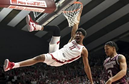 Feb 3, 2024; Tuscaloosa, Alabama, USA;  Alabama forward Mohamed Wague (11) hangs on the rim with a huge smile after dunking over Mississippi State guard Shakeel Moore (3) at Coleman Coliseum. Mandatory Credit: Gary Cosby Jr.-USA TODAY Sports