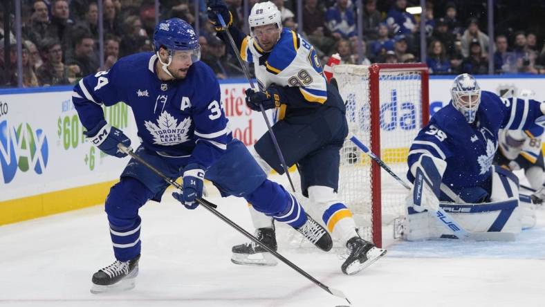 Feb 13, 2024; Toronto, Ontario, CAN; Toronto Maple Leafs forward Auston Matthews (34) goes to clear a rebound as St. Louis Blues forward Pavel Buchnevich (89) looks on during the second period Scotiabank Arena. Mandatory Credit: John E. Sokolowski-USA TODAY Sports