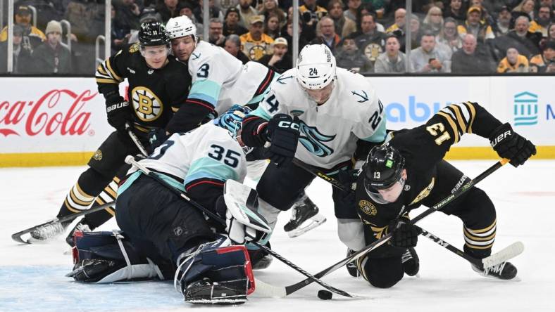 Feb 15, 2024; Boston, Massachusetts, USA; Boston Bruins center Charlie Coyle (13) battles for the puck against Seattle Kraken goaltender Joey Daccord (35) and defenseman Jamie Oleksiak (24) during the first period at TD Garden. Mandatory Credit: Brian Fluharty-USA TODAY Sports