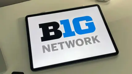 Big Ten Network logo on an iPad sitting on a desk next to a MacBook
