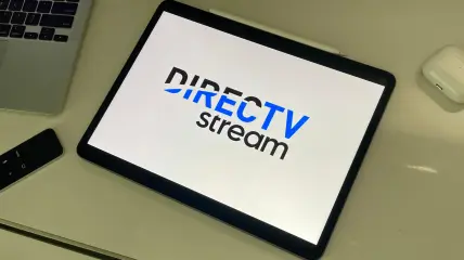 DIRECTV STREAM logo on an iPad sitting on a desk with apple tv remote and AirPods