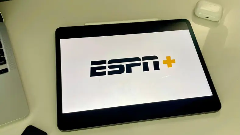 ESPN Plus logo on iPad next to MacBook and AirPods