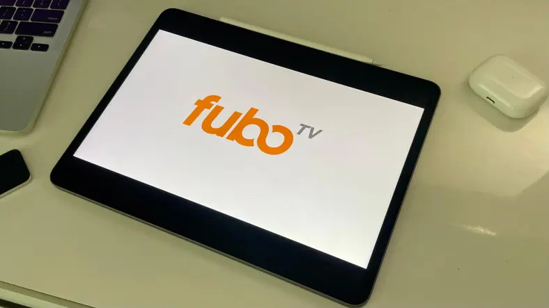 fubo logo on an iPad next to a MacBook and AirPods