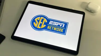 SEC Network logo on an iPad sitting on a desk next to a MacBook and AppleTV remote