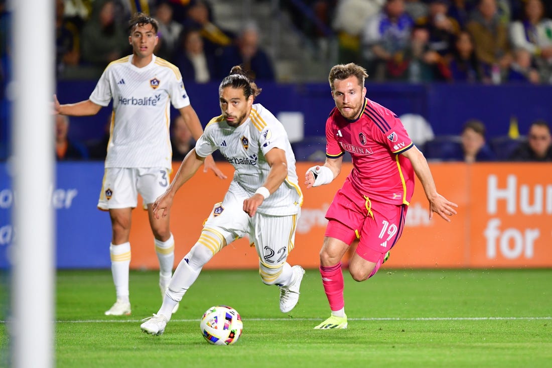 Mar 16, 2024; Carson, California, USA; LA Galaxy defender Martin Caceres (22) and St. Louis CITY SC midfielder Indiana Vassilev (19) chase down the ball during the first half at Dignity Health Sports Park. Mandatory Credit: Gary A. Vasquez-USA TODAY Sports