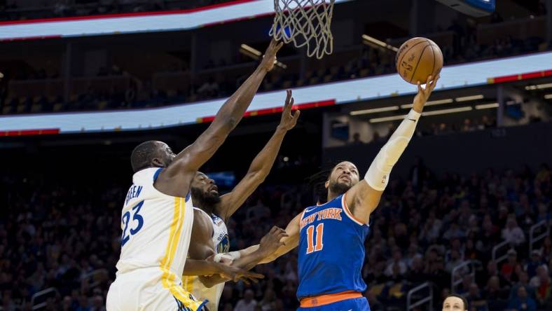 Mar 18, 2024; San Francisco, California, USA;  New York Knicks guard Jalen Brunson (11) shoots as Golden State Warriors center Draymond Green (23) and forward Andrew Wiggins (22) defend during the first half at Chase Center. Mandatory Credit: John Hefti-USA TODAY Sports