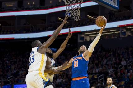 Mar 18, 2024; San Francisco, California, USA;  New York Knicks guard Jalen Brunson (11) shoots as Golden State Warriors center Draymond Green (23) and forward Andrew Wiggins (22) defend during the first half at Chase Center. Mandatory Credit: John Hefti-USA TODAY Sports