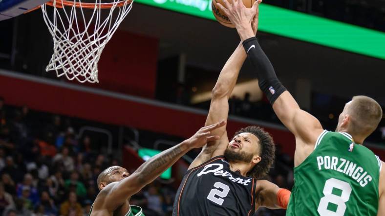 Mar 22, 2024; Detroit, Michigan, USA; Detroit Pistons guard Cade Cunningham (2) gets fouled while driving to the basket against  Boston Celtics forward Xavier Tillman (26) and  center Kristaps Porzingis (8) in the first quarter at Little Caesars Arena. Mandatory Credit: Lon Horwedel-USA TODAY Sports