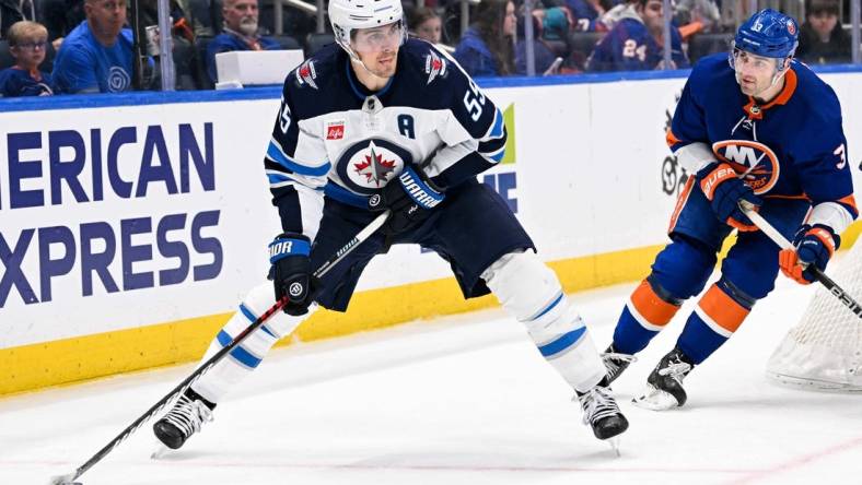 Mar 23, 2024; Elmont, New York, USA;  Winnipeg Jets center Mark Scheifele (55) skates with the puck chased by New York Islanders defenseman Adam Pelech (3) during the third period at UBS Arena. Mandatory Credit: Dennis Schneidler-USA TODAY Sports