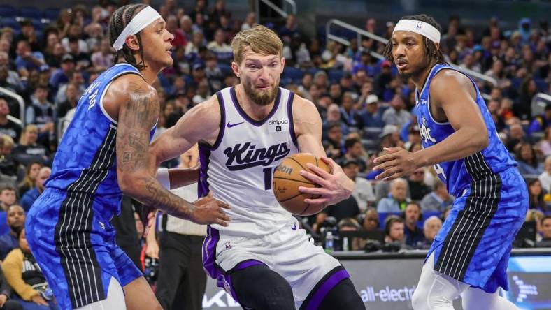 Mar 23, 2024; Orlando, Florida, USA; Sacramento Kings forward Domantas Sabonis (10) drives to the basket against Orlando Magic forward Paolo Banchero (5) and Orlando Magic center Wendell Carter Jr. (34) during the first quarter at KIA Center. Mandatory Credit: Mike Watters-USA TODAY Sports