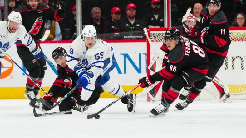 Mar 24, 2024; Raleigh, North Carolina, USA;  Carolina Hurricanes defenseman Brett Pesce (22) and left wing Teuvo Teravainen (86) battle Toronto Maple Leafs left wing Tyler Bertuzzi (59) for the puck during the first period at PNC Arena. Mandatory Credit: James Guillory-USA TODAY Sports