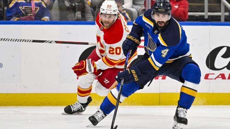 Mar 28, 2024; St. Louis, Missouri, USA;  St. Louis Blues defenseman Nick Leddy (4) controls the puck as Calgary Flames center Blake Coleman (20) gives chase during the first period at Enterprise Center. Mandatory Credit: Jeff Curry-USA TODAY Sports