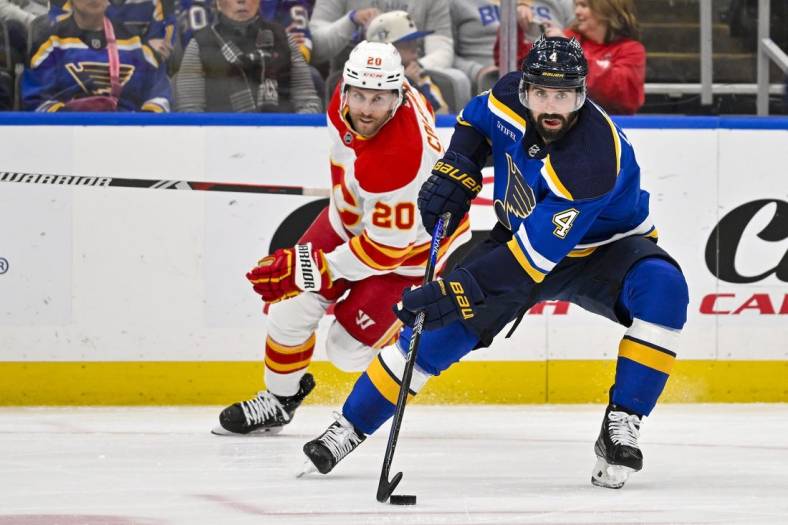 Mar 28, 2024; St. Louis, Missouri, USA;  St. Louis Blues defenseman Nick Leddy (4) controls the puck as Calgary Flames center Blake Coleman (20) gives chase during the first period at Enterprise Center. Mandatory Credit: Jeff Curry-USA TODAY Sports