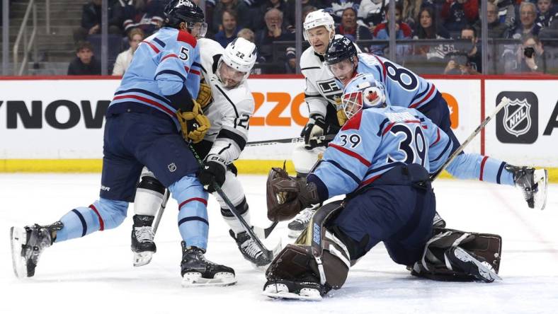 Apr 1, 2024; Winnipeg, Manitoba, CAN; Winnipeg Jets defenseman Brenden Dillon (5) and Los Angeles Kings left wing Kevin Fiala (22) scramble for the puck in front of Winnipeg Jets goaltender Laurent Brossoit (39) in the first period at Canada Life Centre. Mandatory Credit: James Carey Lauder-USA TODAY Sports