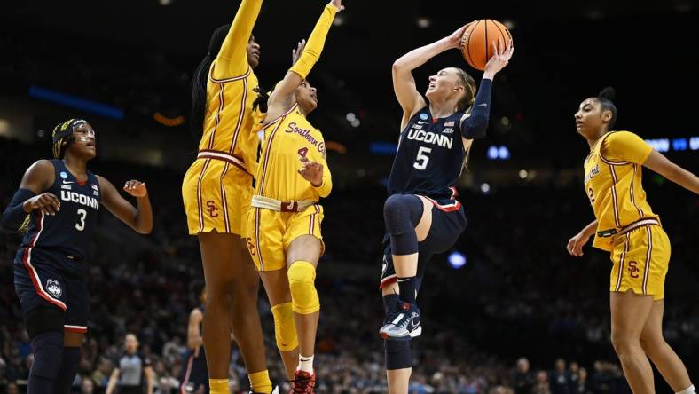 Apr 1, 2024; Portland, OR, USA; UConn Huskies guard Paige Bueckers (5) drives to the basket during the first half against USC Trojans guard Kayla Williams (4) and center Clarice Akunwafo (34)in the finals of the Portland Regional of the NCAA Tournament at the Moda Center. Mandatory Credit: Troy Wayrynen-USA TODAY Sports