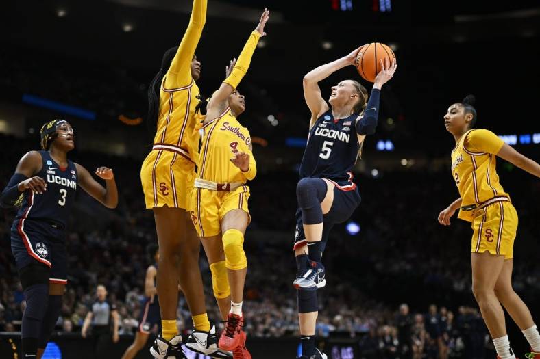 Apr 1, 2024; Portland, OR, USA; UConn Huskies guard Paige Bueckers (5) drives to the basket during the first half against USC Trojans guard Kayla Williams (4) and center Clarice Akunwafo (34)in the finals of the Portland Regional of the NCAA Tournament at the Moda Center. Mandatory Credit: Troy Wayrynen-USA TODAY Sports