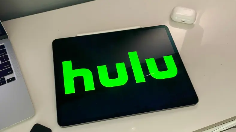 Hulu logo on an iPad sitting next to a MacBook and AirPods