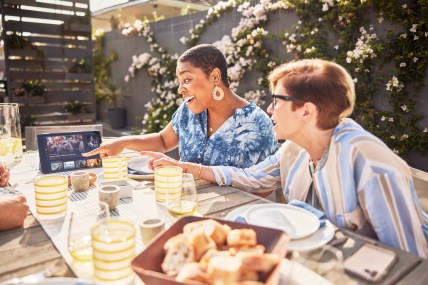 Two Girlfriends Watching Sling TV On Their Tablet While Eating On Their Patio